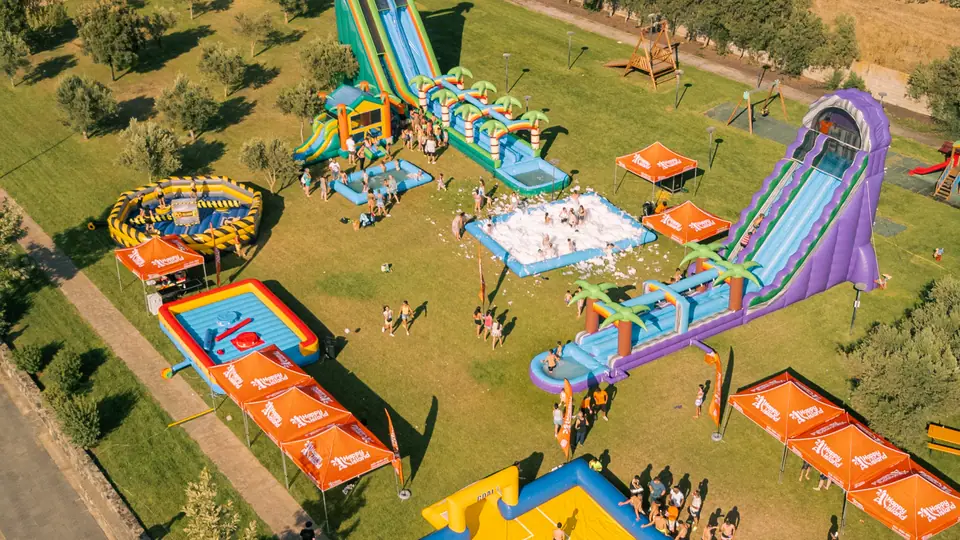 Vista dall'alto di un Acqua Party Happy Island con scivoli ad acqua, gonfiabili, gazebo arancioni e bambini in piazza